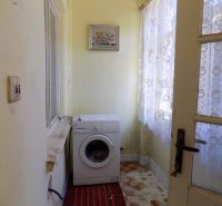 A small room with a washing machine, tiled floor, and curtains, suitable for a family house.