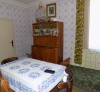 A dining room of a family house with a patterned tablecloth, wooden furniture, and a tiled wall.
