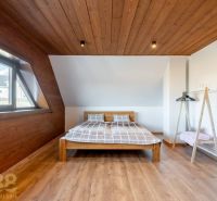 A bedroom in a family house with a bed, a wooden decor floor, and wooden walls.