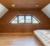 Attic bedroom in a family house with a wooden decor floor and large windows.