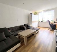 Living room in a three-room apartment with a wooden decor floor, a sofa, and a table.