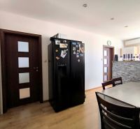A kitchen in a 3-room apartment with a dining table, a black refrigerator, and a wooden decor floor.