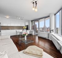 Living room and kitchen in a 3-room apartment with a wooden decor floor, large windows, and a sofa.