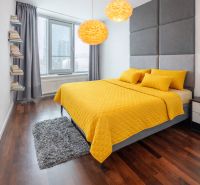 A bedroom in a 3-room apartment with a wooden decor floor and yellow bed linen.