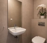 Bathroom with a sink, mirror, and toilet in a 3-room apartment with light-colored tiles.