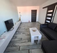 A living room with a black sofa, a white table, and a wooden decor floor in a three-room apartment.