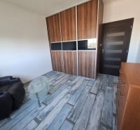 A room with a sofa, a wardrobe, a table, and a floor with a wooden decor in a 3-room apartment.