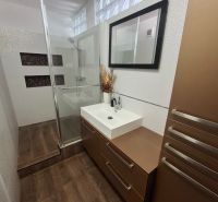 A bathroom with a shower, a mirror, and a wooden decor floor in a 3-room apartment.
