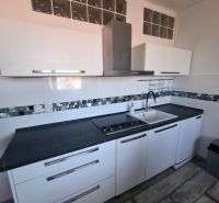 A kitchen in a 3-room apartment with glossy white cabinets and a dark countertop.