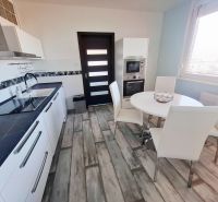 A kitchen in a 3-room apartment with white furniture and a wooden decor floor.