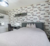 A bedroom with a feature wall with a pattern of inscriptions, next to a wardrobe and a desk.