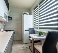 A kitchen in a 2-room apartment with a table, chairs, a kitchen unit, and a refrigerator, with a wooden decor floor.