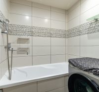 A bathroom with a bathtub, a washing machine, and tiles in a 2-room apartment.