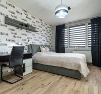 A bedroom in a two-room apartment with a bed, a desk, and a wooden decor floor.