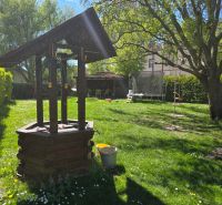 A garden with a wooden well, a trampoline, and a swing rope under a tree.