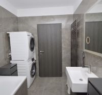 A bathroom in a family house with a washing machine, dryer, and bathtub, gray tiles.
