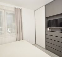 A bedroom in a family house with a television, a wardrobe, and a large window with curtains.