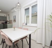 Dining room in a family house with a white table, pink chairs, and a green kitchen.