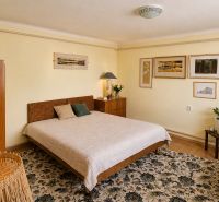 Bedroom in a family house with a blanket, wooden furniture, and artistic paintings on the wall.