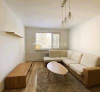 Living room with a beige corner sofa, wood-patterned flooring, and a wall shelf.