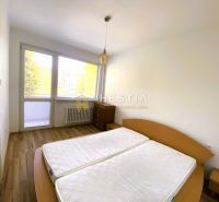 Bedroom in a two-room apartment with a wood-patterned floor and a large window.