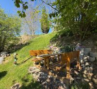 A garden in Čaradice by a family house with wooden seating under a tree.