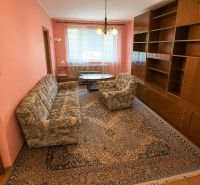 Living room in a 3-room apartment with pink walls, patterned carpet, and wooden cabinets.