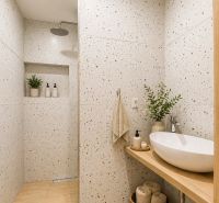 The bathroom of a 2-room apartment with terrazzo walls, a shower corner, and cozy decoration.