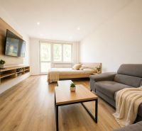 A bright living room with a TV on the wall in a 2-room apartment with wooden floor decor.