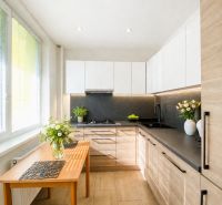 A kitchen in a 2-room apartment with a wooden decor floor and white cabinets.