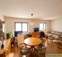 Living room with a sofa, windows, table, and wooden decor flooring in a family house.