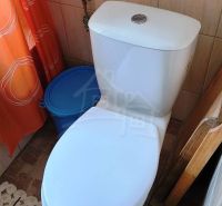 A toilet in a family house, with an orange curtain and a blue bucket.