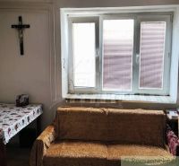 A room in a family house with a sofa, a table with a cloth, and a cross on the wall.