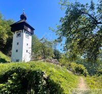 In Žarnovica, next to the Chata, there is a tall tower surrounded by greenery and a blue sky.