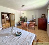The interior of a cabin with a wooden decor floor, a table, and a tiled stove.