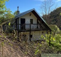 A cottage in Žarnovica, set in the forest, with a wooden balcony and grassy surroundings.