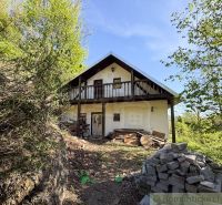 A cottage in Žarnovica surrounded by greenery with a wooden balcony and a pile of bricks.