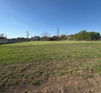 A flat plot of land in Pozba designated for residential use, with a view of neighboring houses.