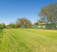 A grassy residential plot on Nová Street in Viničné, bordered by trees and a fence.