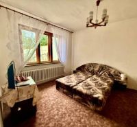 A bedroom in a family house with carpeted flooring and two beds, illuminated by a window.