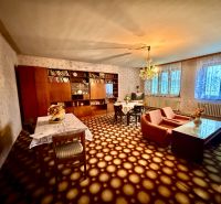 A living room in a family house with carpeted flooring, retro furniture, and a chandelier.
