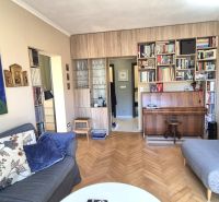 Living room in a two-room apartment with a piano, sofas, and a wooden decor floor.