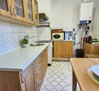A kitchen in a 2-room apartment with wooden furniture, white tiles, and a table with fruit.