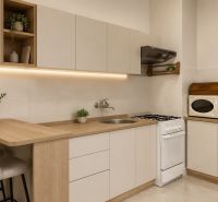 A kitchen with beige cabinets, a microwave, and bar stools in a two-room apartment.