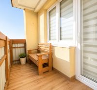 A balcony of a 3-room apartment with wooden seating and flooring with a wooden decor.