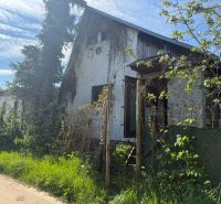 An abandoned cabin in the town of Malacky surrounded by greenery and trees.