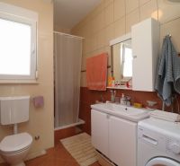 A bathroom in a family house with a sink, a washing machine, and a shower stall.