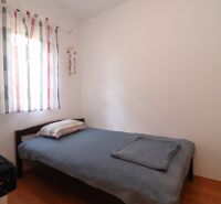 Simple bedroom with a bed, wood-patterned flooring, and light curtains.