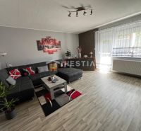A spacious living room in a three-room apartment with a wooden decor floor and a comfortable sofa set.