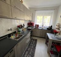 A kitchen with a kitchen unit, table, and floor with a wooden decor in a 3-room apartment.